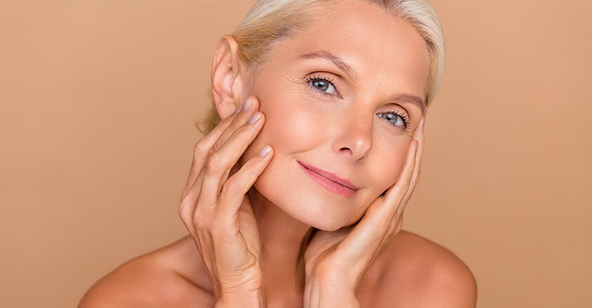 Uśmiechnięta kobieta zastanawiająca się, jak odmłodzić twarz po 50. roku życia