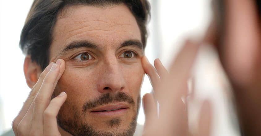 Mężczyzna obserwuje oznaki starzenia skóry wokół oczu i zastanawia się, jaki dobry krem dla mężczyzn będzie odpowiedni