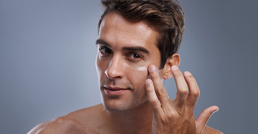 Młody mężczyzna aplikuje krem przeciwzmarszczkowy dla mężczyzn pod oczy