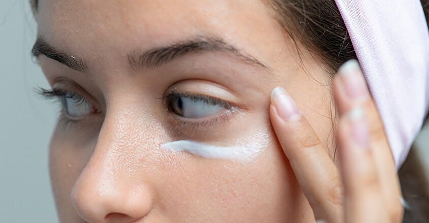 Młoda kobieta aplikuje krem na worki pod oczami