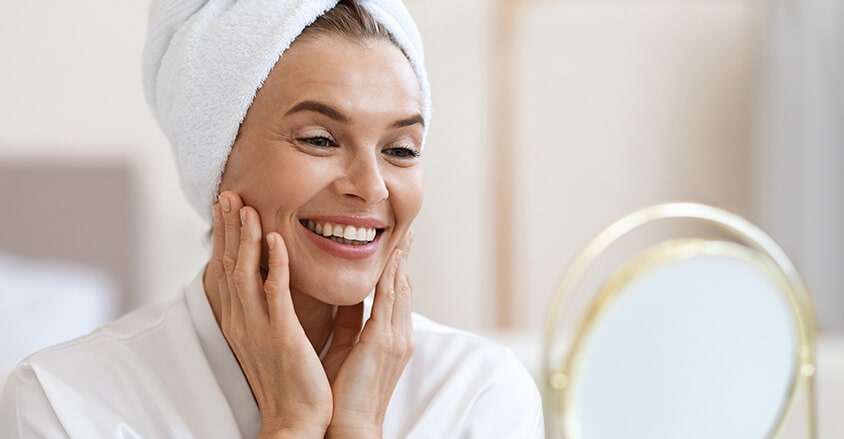 Kobieta przeglądająca się w lustrze i zastanawiająca się jak odmłodzić twarz w domu